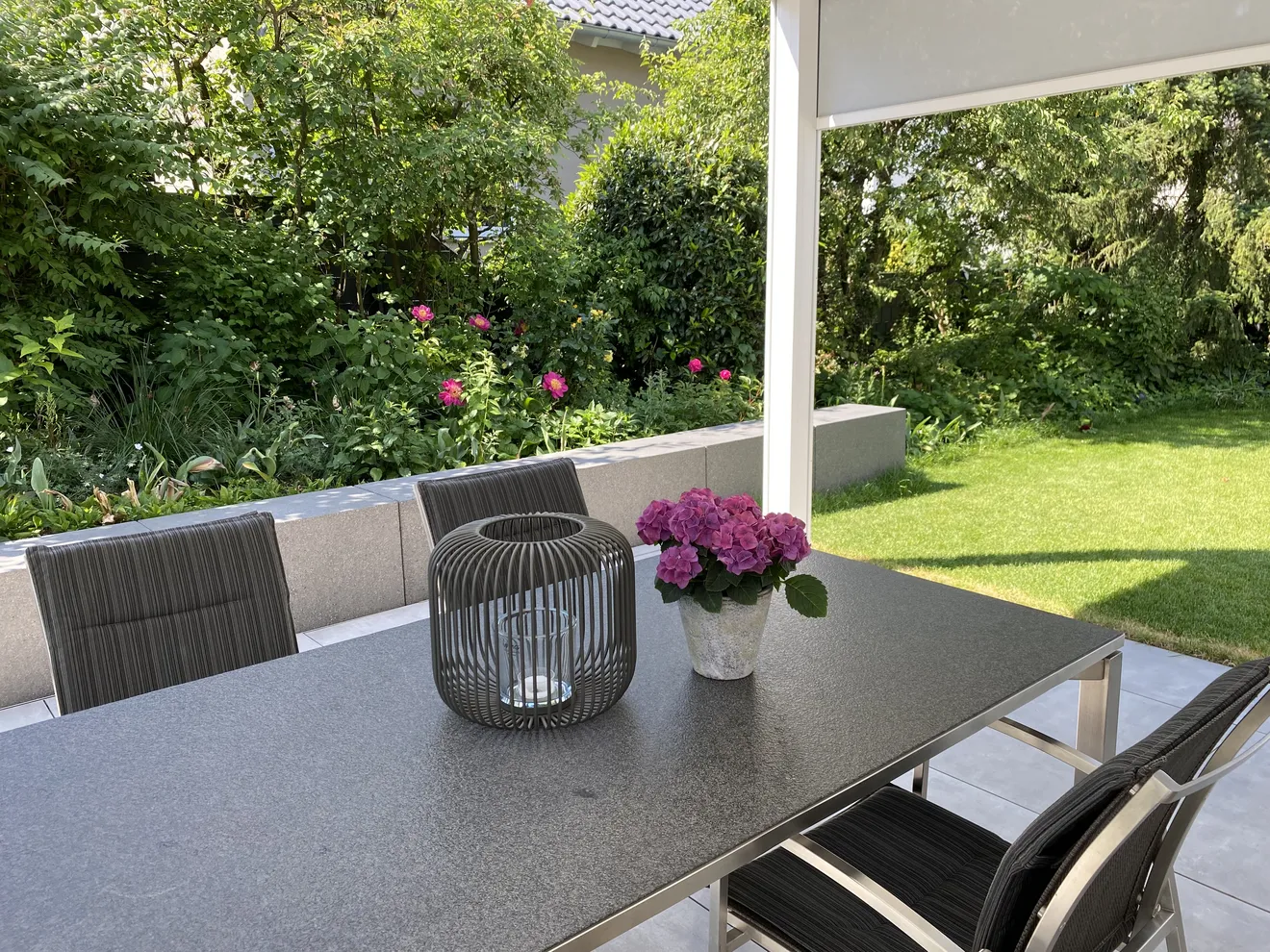 Blick von einer modernen Terrassenüberdachung auf einen privaten Garten mit Sichtschutz, Rasenfläche und Staudenbeeten